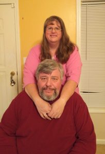 Image of Theresa and John by a yellow wall smiling