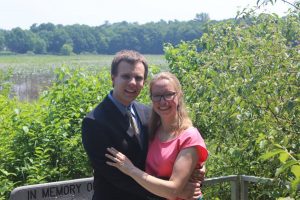 Image of Dominik and Lillian with arms around each other next to green trees and water