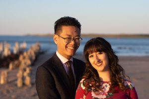 Image of smiling Shelyse and Brandan in front of sand and water