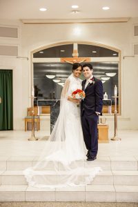 Image of couple standing on altar near crucifix in wedding attire