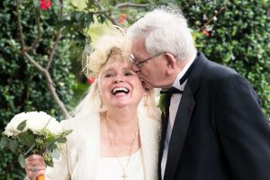 Image of older man kissing older woman on the cheek in a garden.